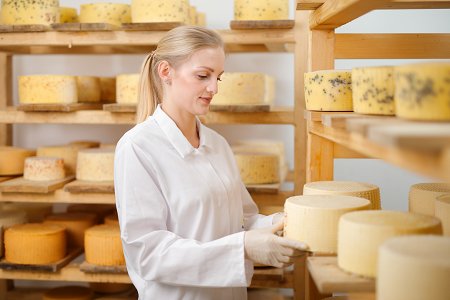 ženska v beli halji sredi sobe polne sirov