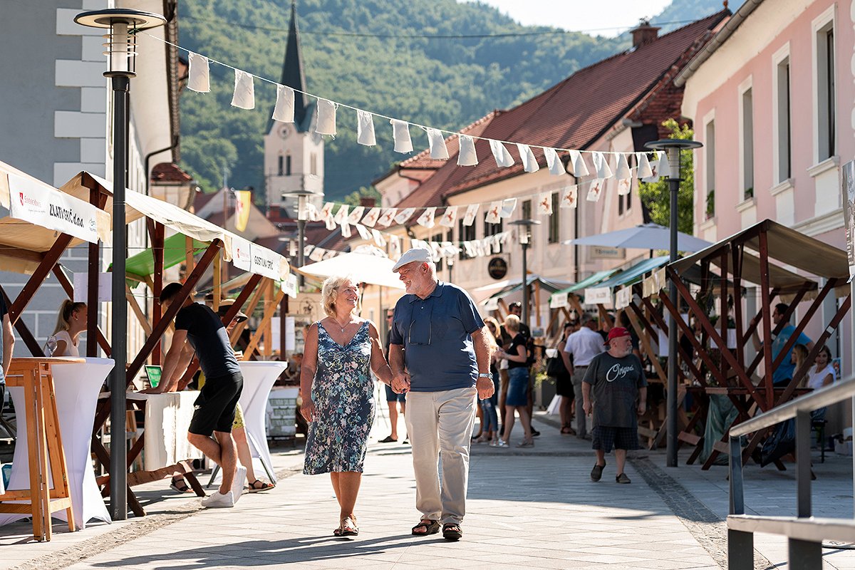 an elderly couple walks down a decorated street with stalls